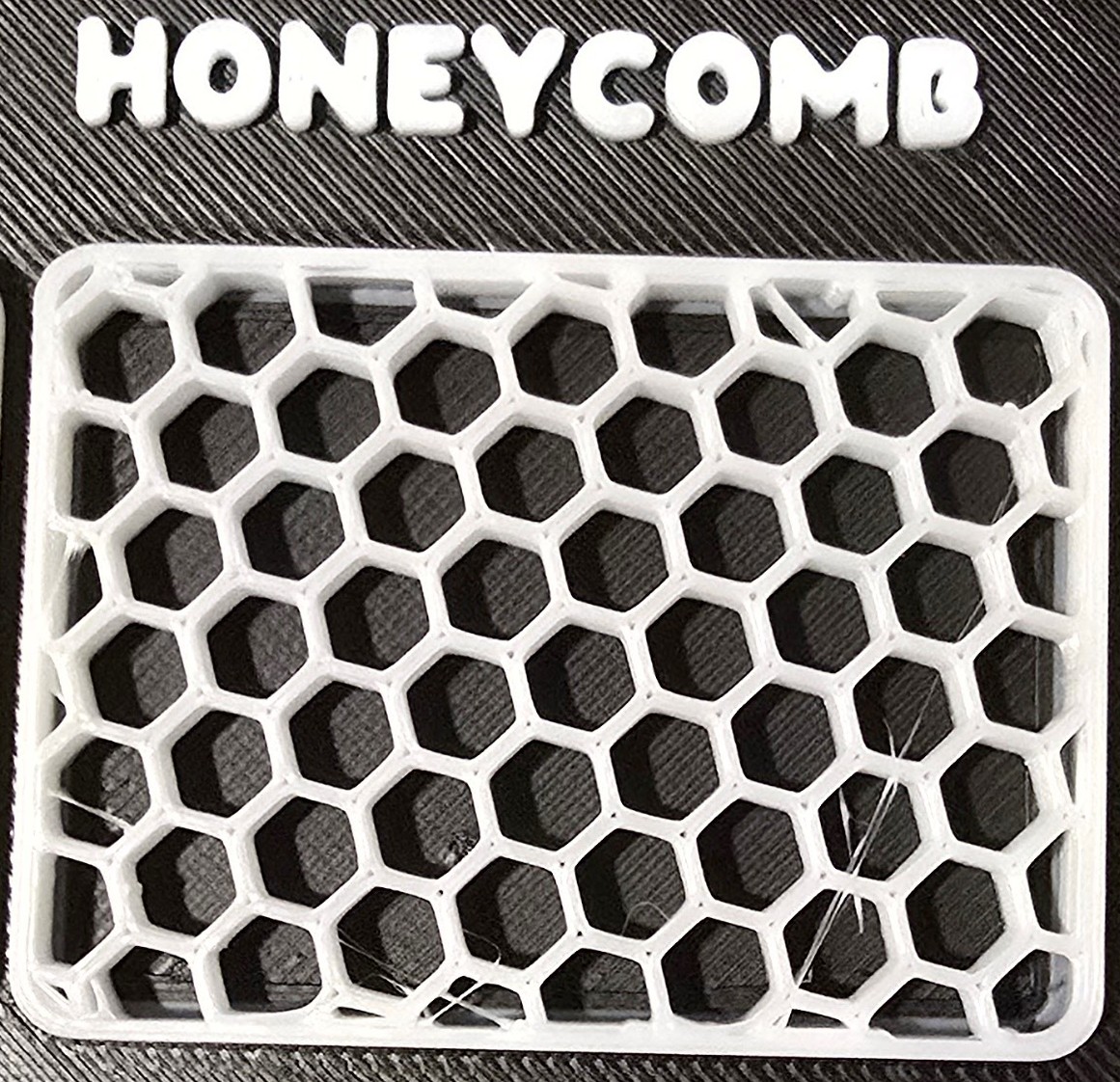 A close-up of honeycomb hexagonal infill with visible fine white stringing across the open cells.